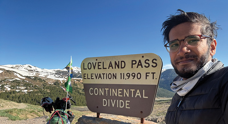 Mufaddal Fidahussein posing with his bike by the Continental Divide sign at Loveland Pass