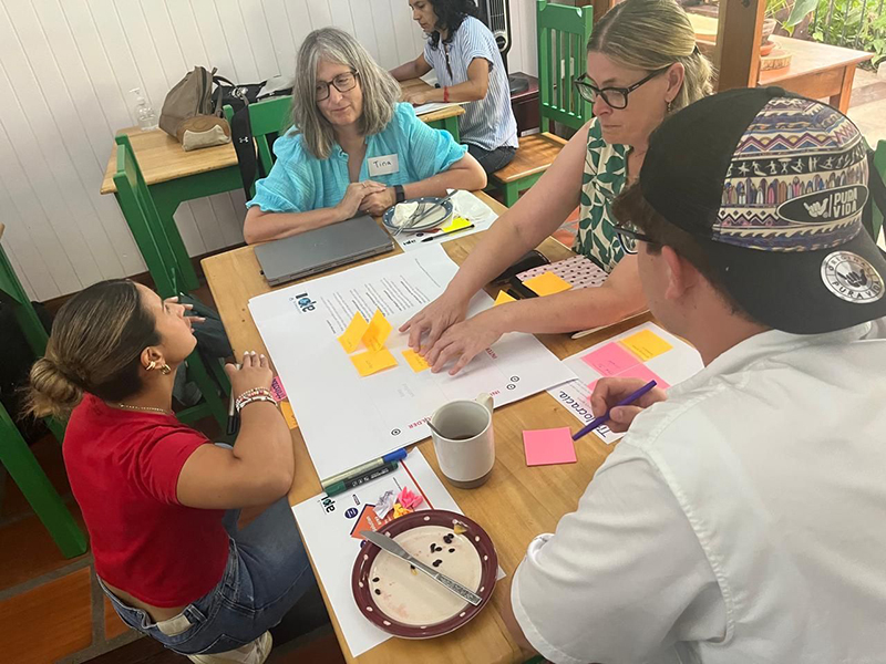 web-edu-exp2 Tina Herzberg at a table with other members of a group visiting Costa Rica